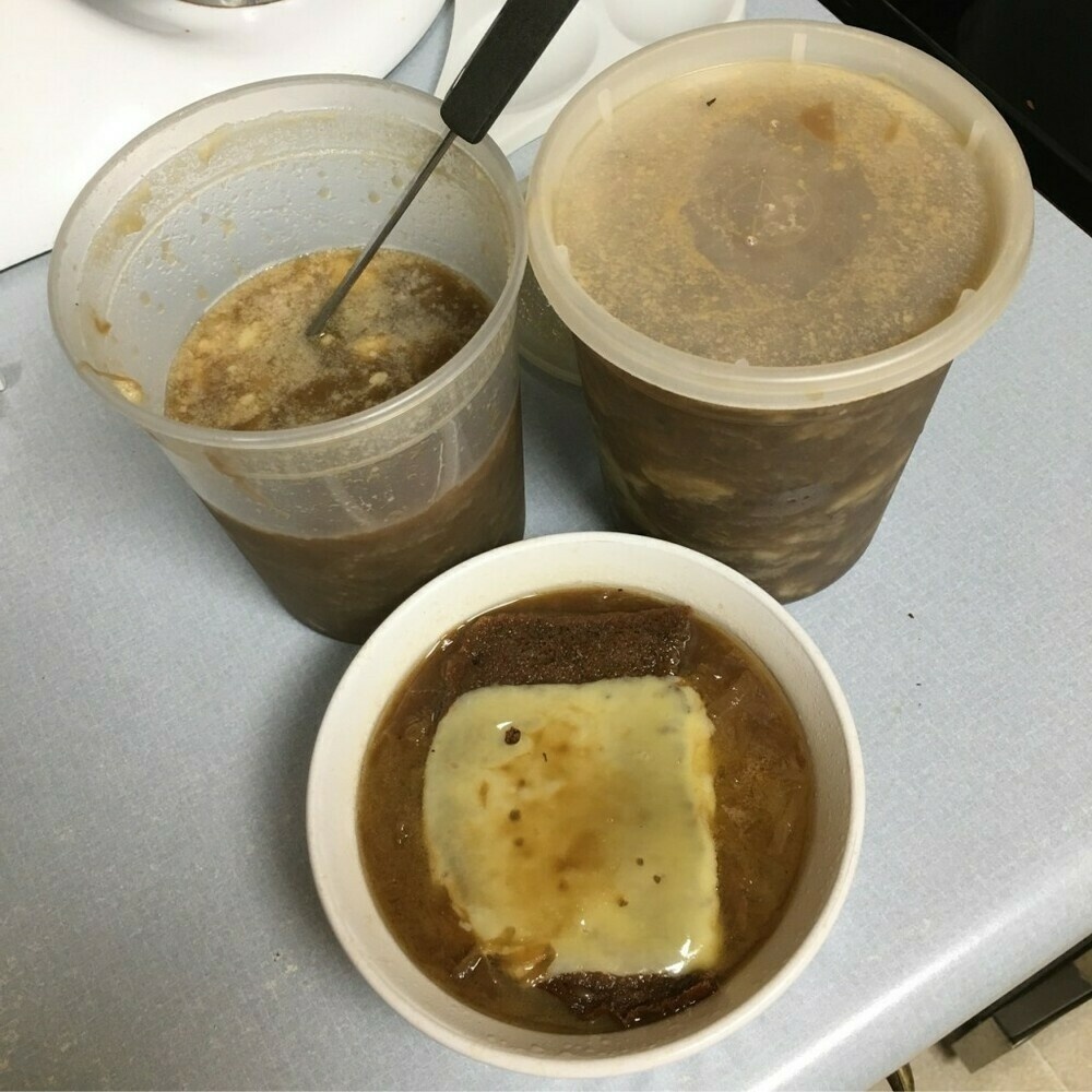 Bowl of homemade French onion soup with bread and cheese in front of two containers of soup.