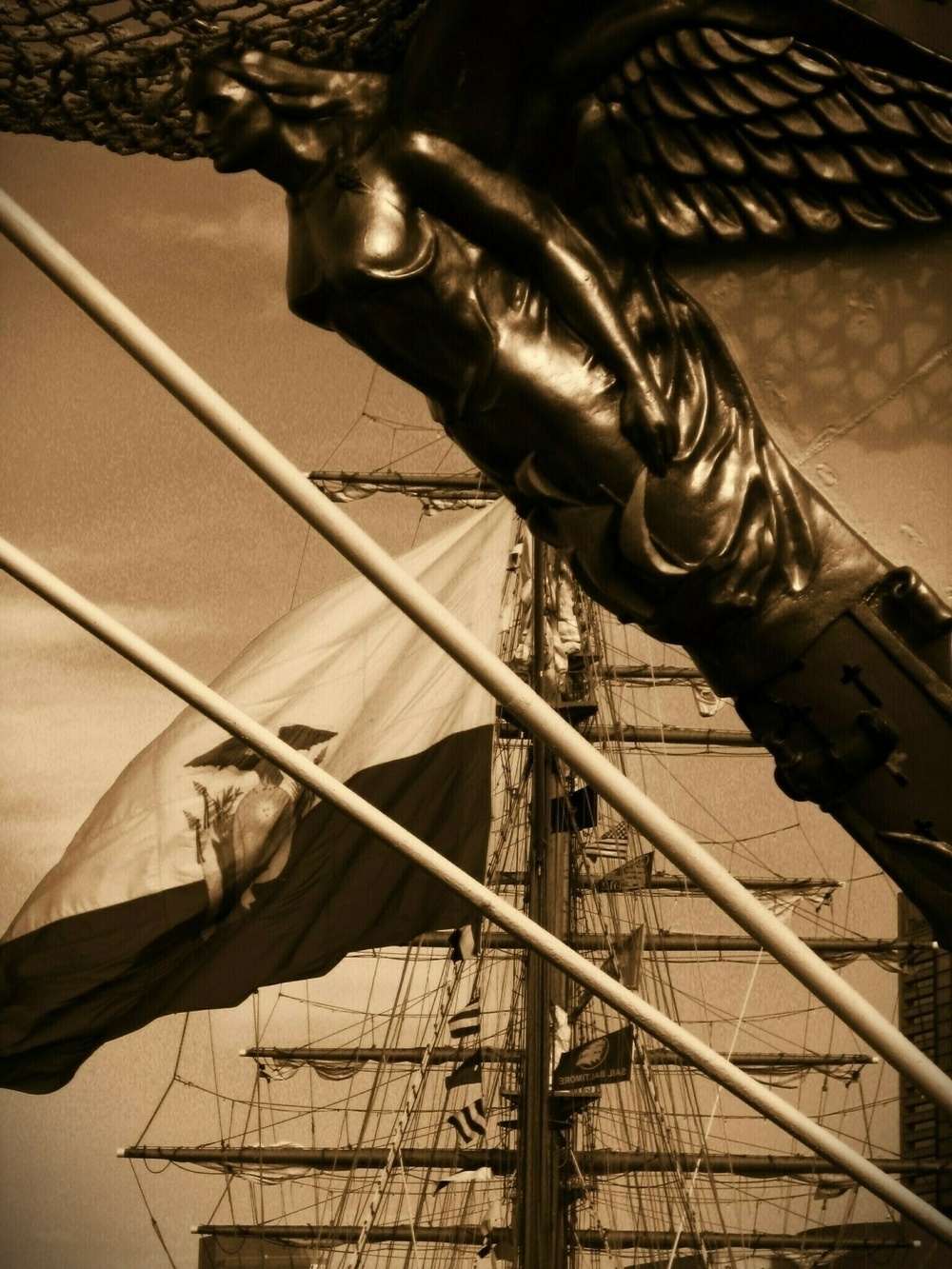 A ship's figurehead with a large flag and sailing ship in the background.