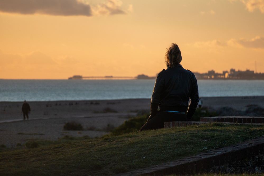A man sits on the edge of Shoreham Fort, watching the sun set over Worthing. 