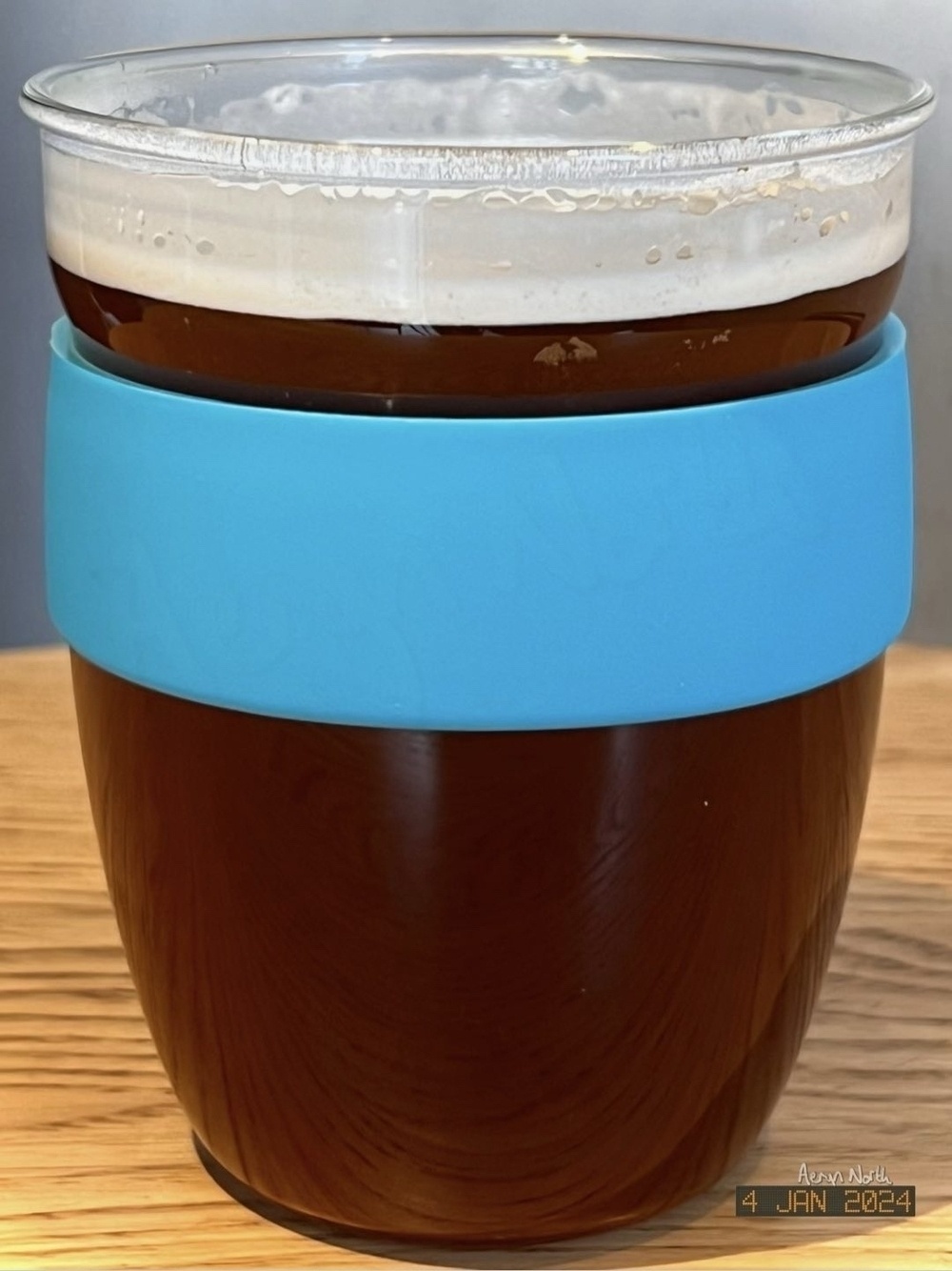 A glass drinking cup with a silicone band around it, containing black coffee. 