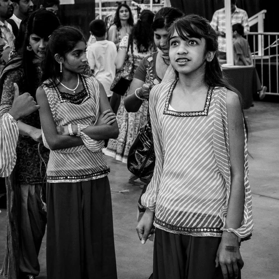 Girls wearing similar striped clothing standing and mingling at an indoor event surrounded by a crowd of people.