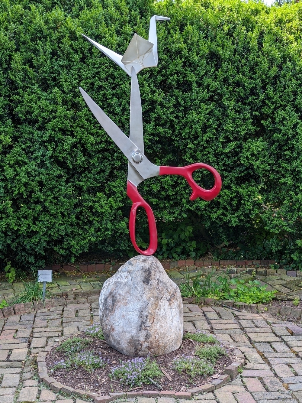 a sculpture of a paper origami crane balanced on a pair of scissors balancing on top of a rock