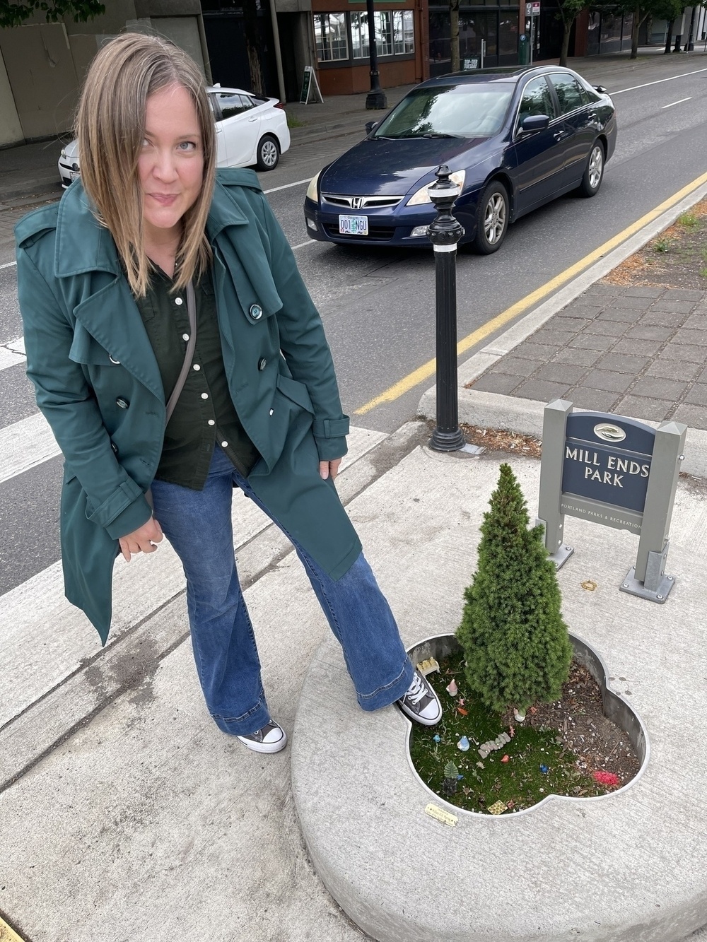 Mills End Park, which is a to tiny tree in a to y cement enclosure. A woman stands by with her foot next to the park for scale.