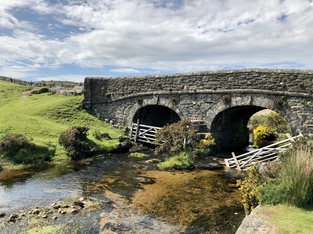 A stone bridge over a creek with mossy grass on the banks