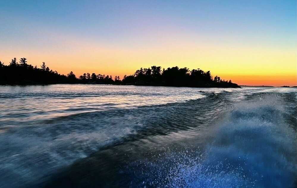 Crashing waves on the lake form the side of a boats Sunset is in the background with silhouette trees at dusk