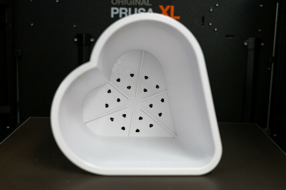 Photo of a 3D printed flower pot in a heart shape. Pointing down to the bottom of the pot, highlighting the heart shaped holes and ribs.