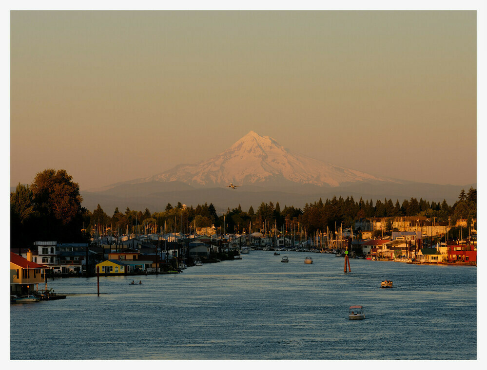 A plane takes off over North Portland Harbor with Mount Hood in the background. The sun is setting, washing the area in an orange glow.