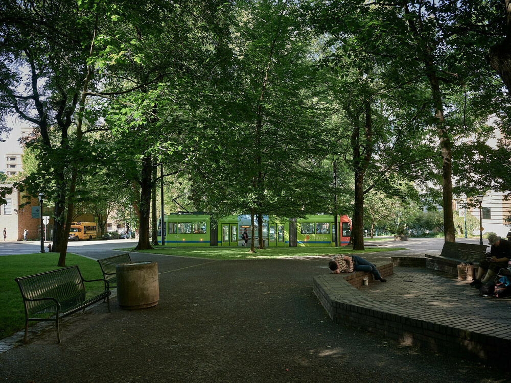 The North-South Portland Streetcar line at Park Avenue and Mill Street in Portland's South Park blocks near Portland State University. People are sitting on park benches, looking at their phones. Another person is taking a nap on a stone pedestal.