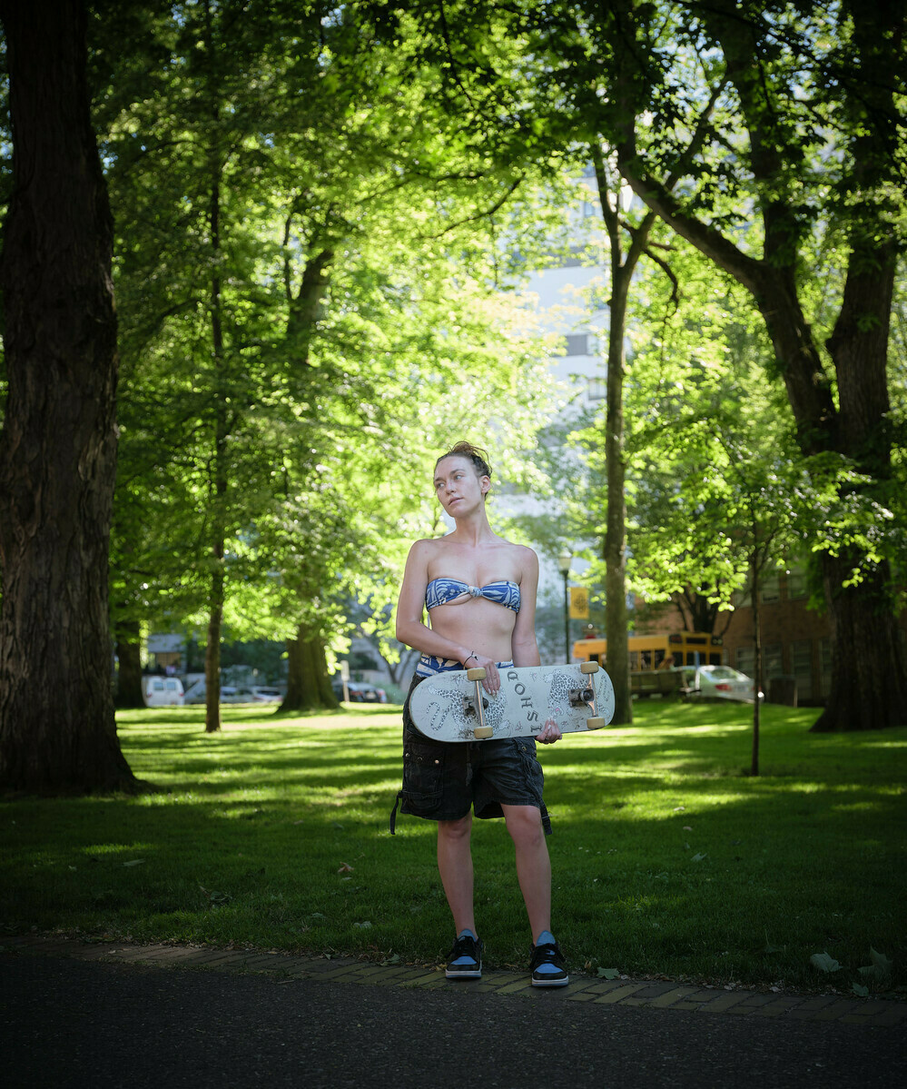 A woman is posing with her skateboard in front of a city park.