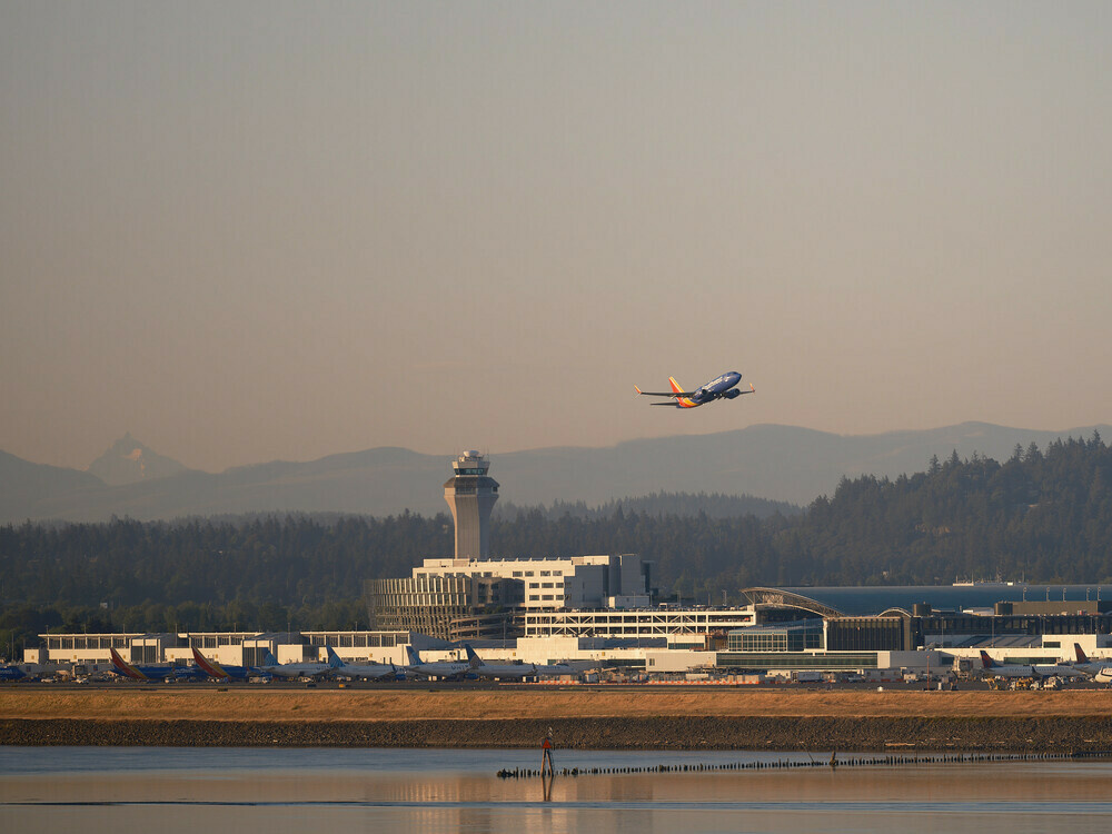 A Southwest Airlines aircraft is taking off from Portland International Airport. The airport facilities, including parked airplanes and the air traffic control tower, make up part of the composition.