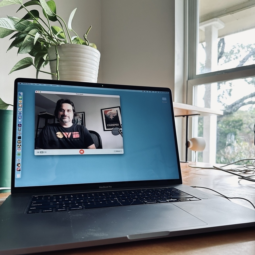 MacBook on a desk with window and plant.