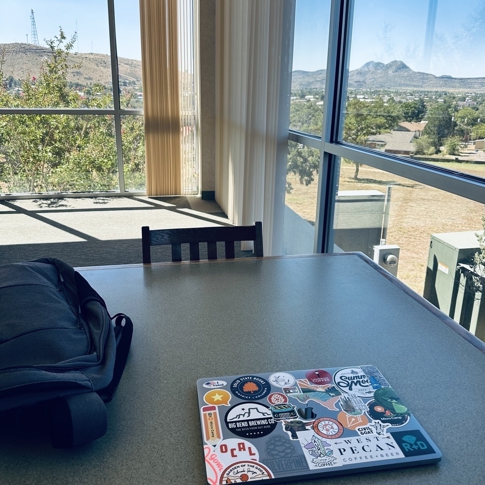 Laptop and bag on table with Alpine TX and mountains out the window.