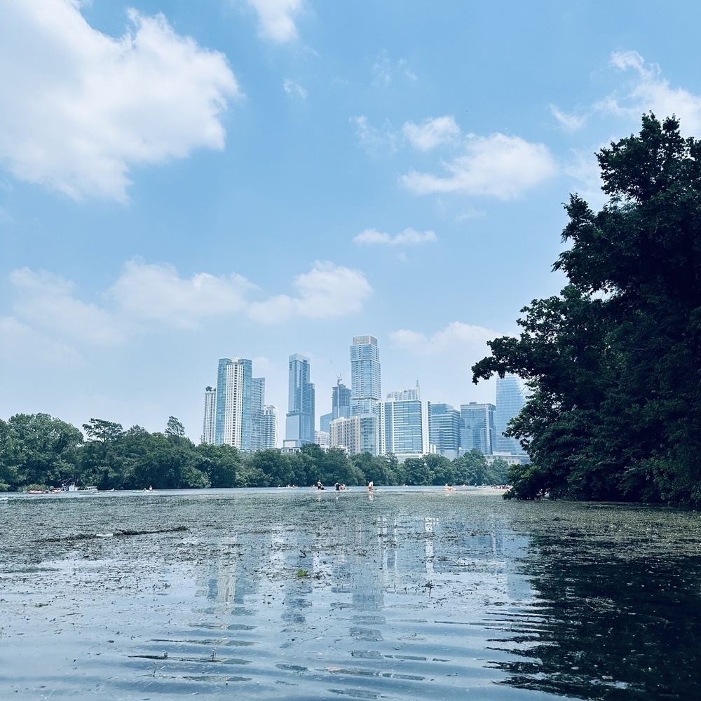 Austin cityscape is visible across Lady Bird Lake with lush trees on the right under a partly cloudy sky.