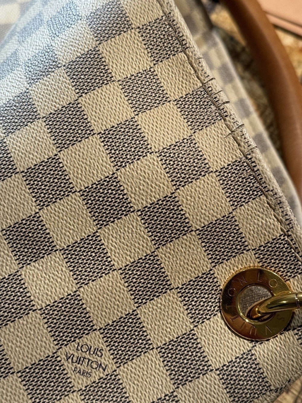 A close-up view of a cracked Louis Vuitton checkered fabric accessory with a circular metal ring is shown.
