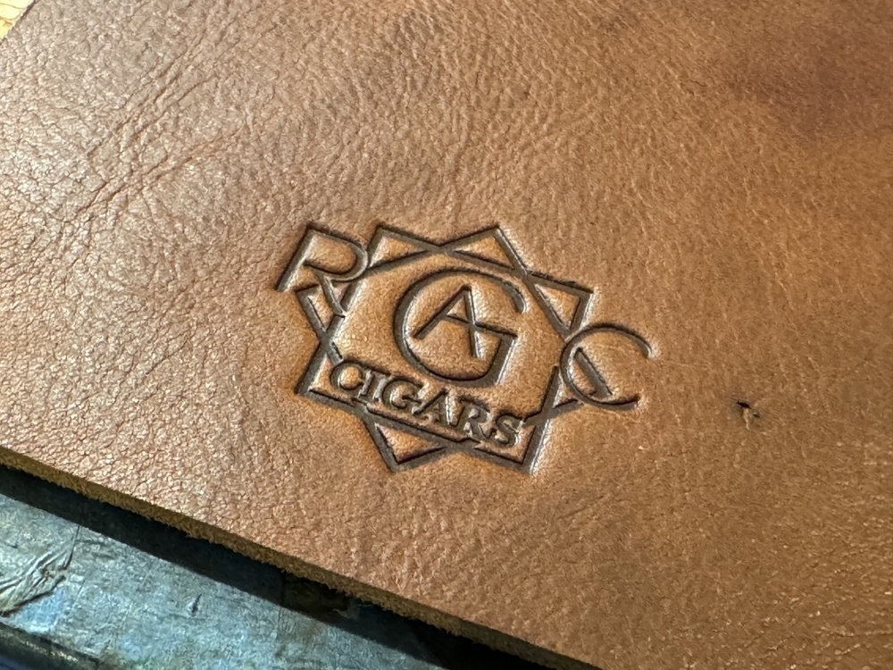 A piece of leather features an embossed logo with a geometric design and the text "CIGARS".