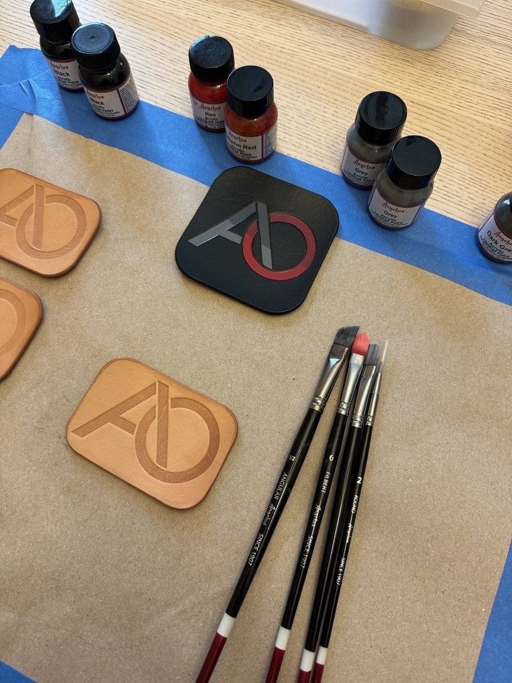 A workspace featuring painted coasters with a logo, paintbrushes, and small jars of paint.