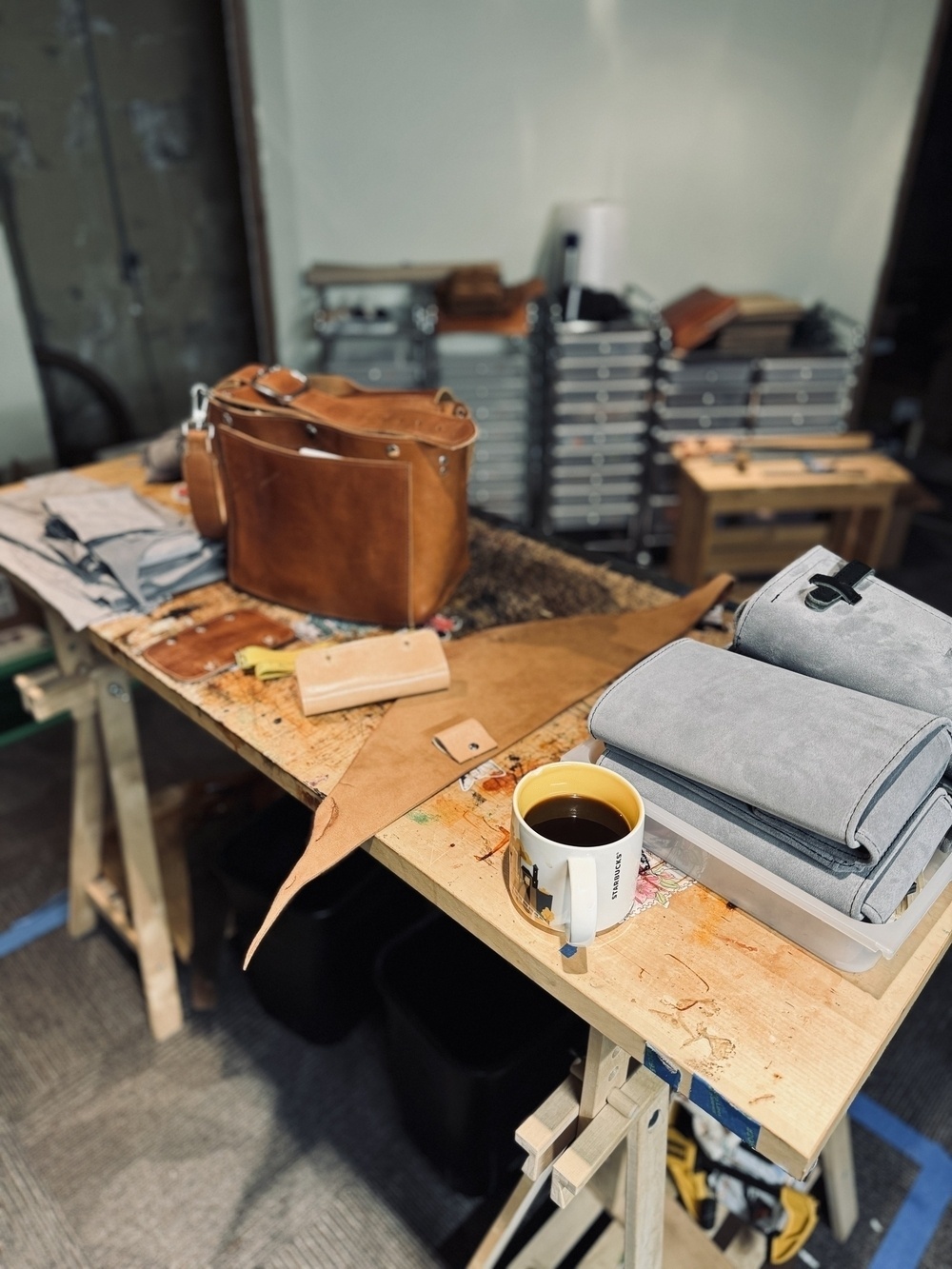 A workbench features leather crafting materials, including a partially constructed bag and a mug.