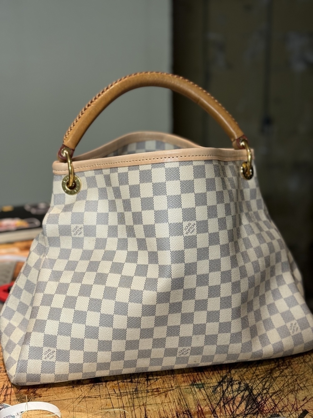 A checkered handbag with a tan handle is placed on a wooden surface.