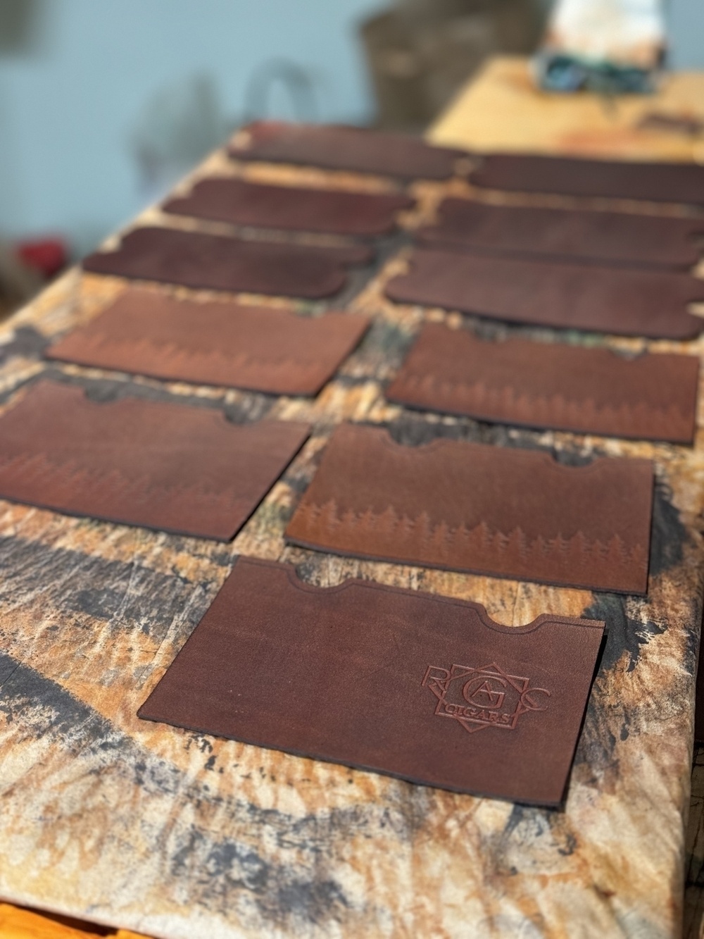 A workbench is covered with several pieces of rectangular brown leather, some of which feature a debossed logo.