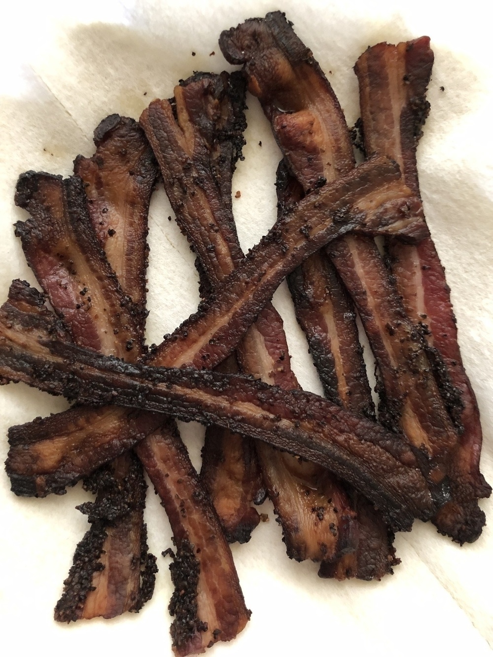 A plate of thickly cut pepper bacon cooked to a crisp.