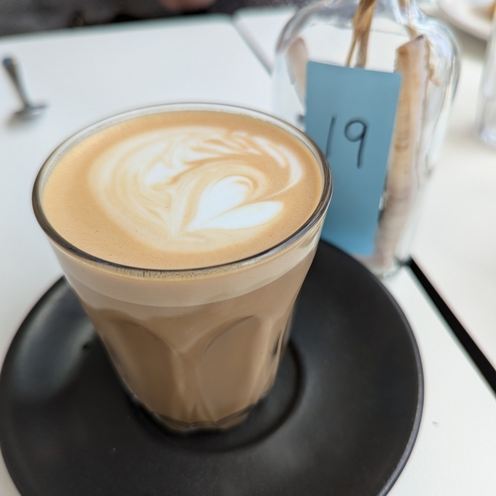 A latte in a glass is topped with a foam art heart