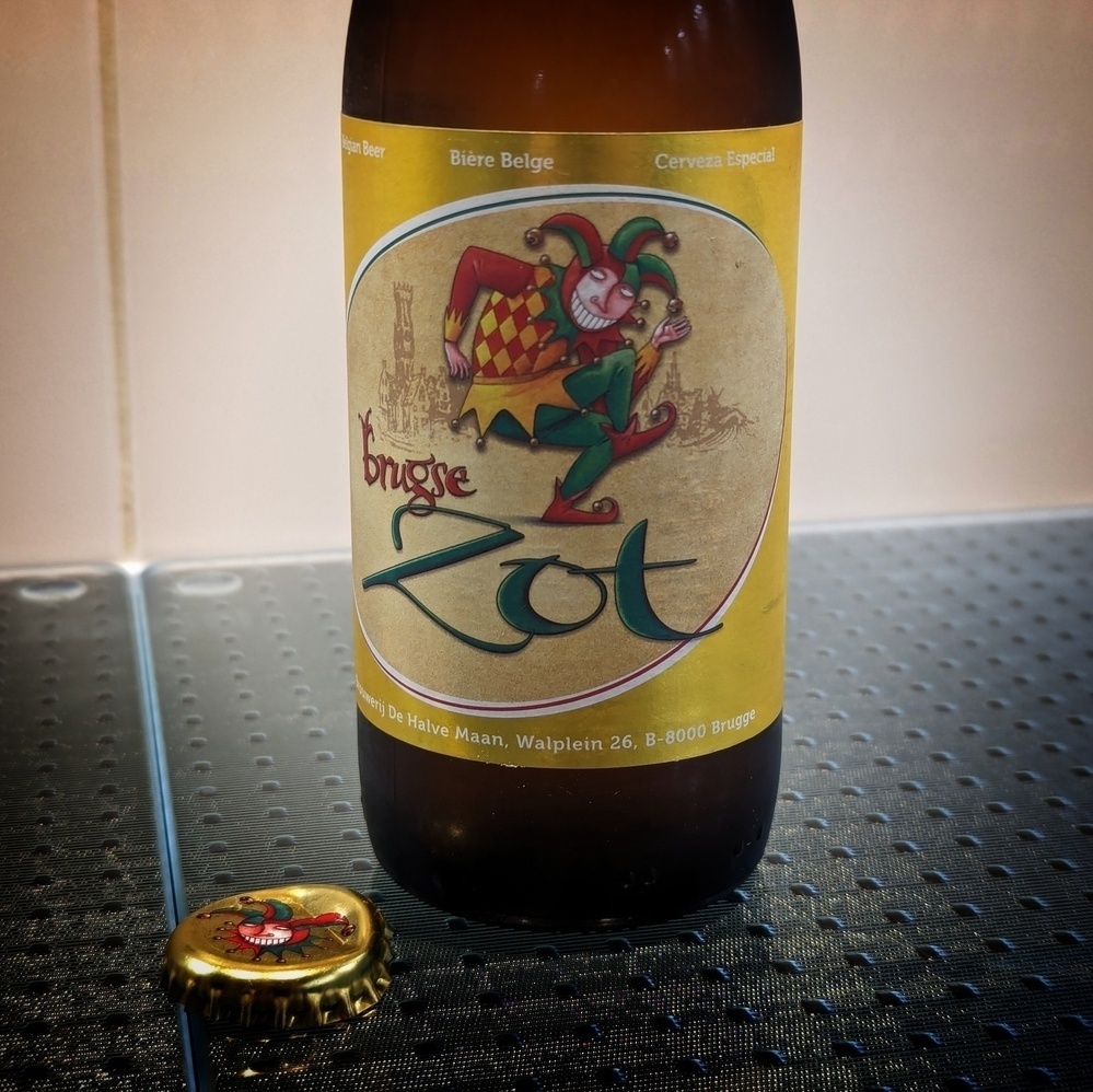 A bottle of Brugse Zot Blond beer alongside it’s removed cap