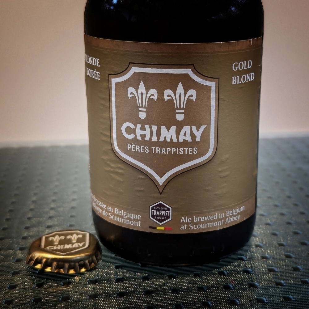 A bottle of Chimay Gold beer next to it’s cap