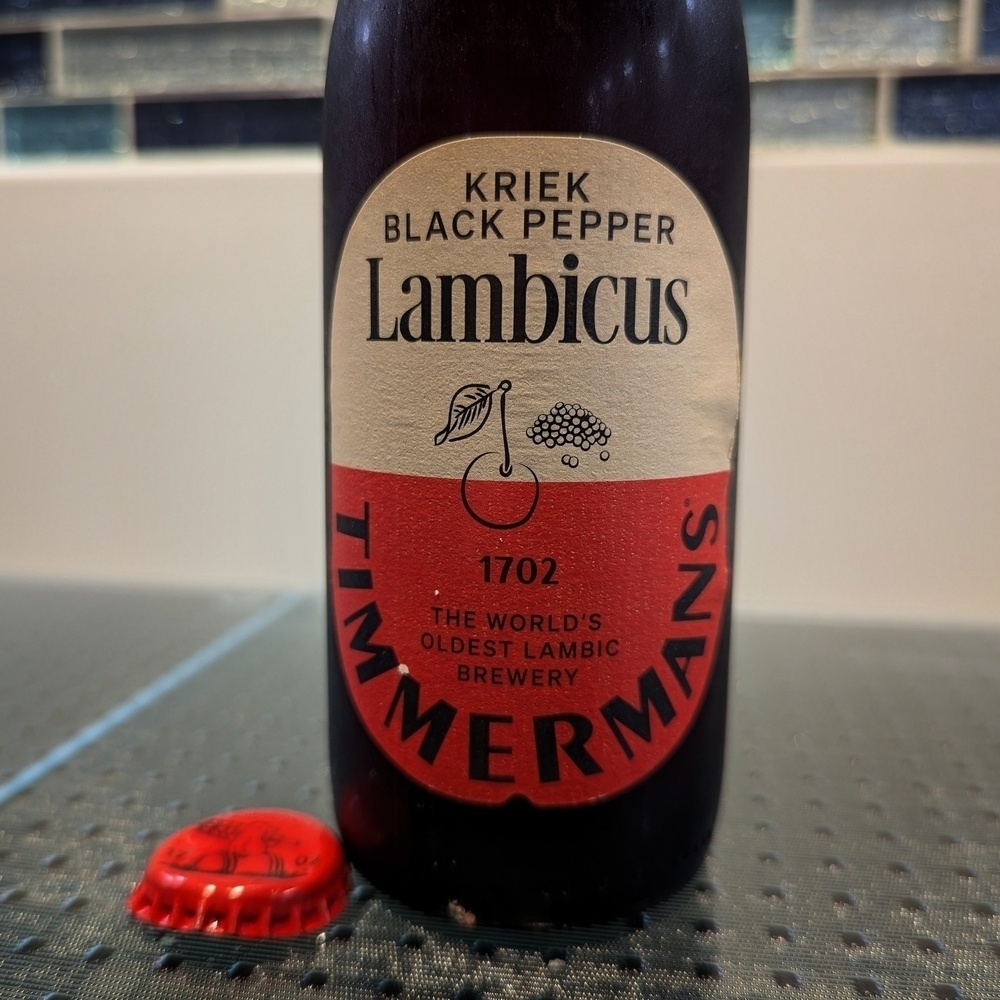 A bottle of Timmermans Kriek Black Pepper beer besides it’s removed cap.