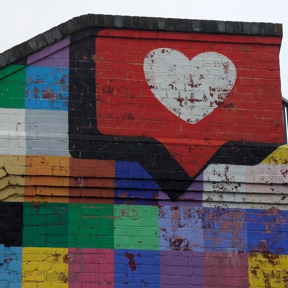 Red speech bubble containing a heart sits at the top right of a colourful chequered wall mural