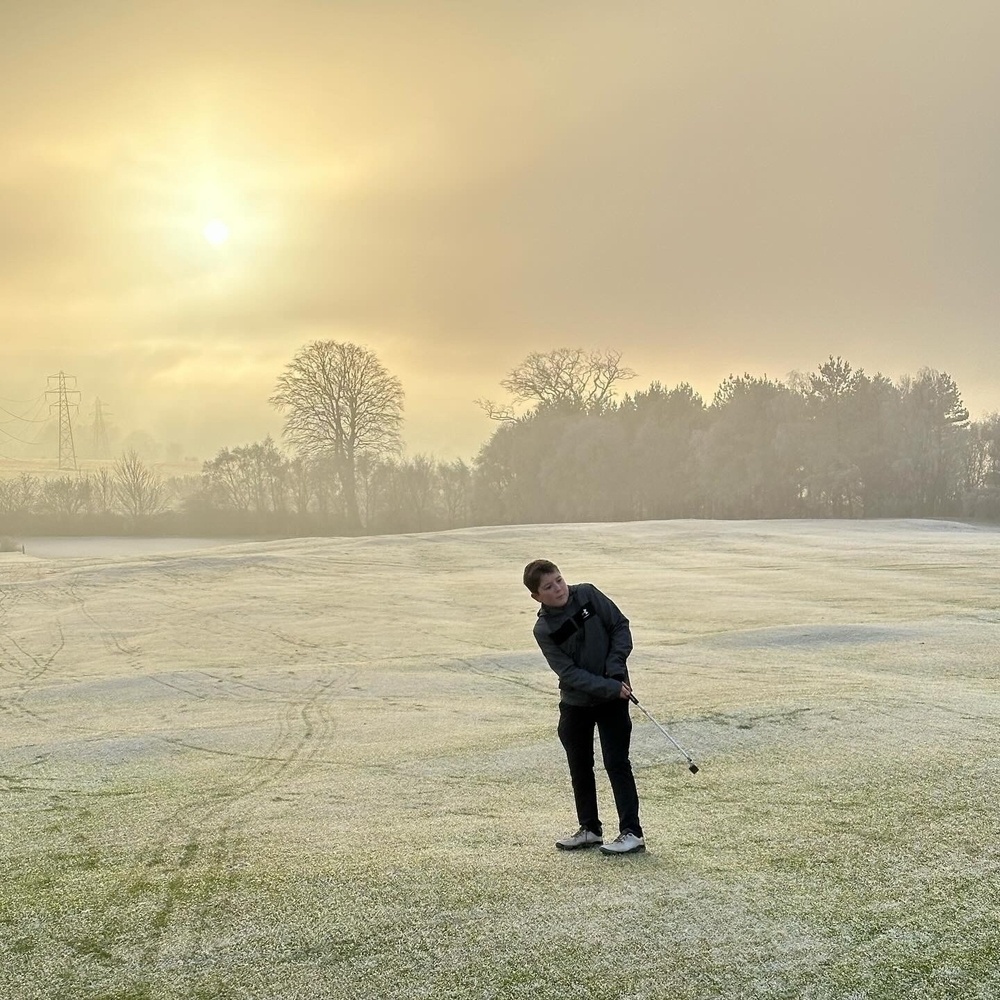 A boy playing golf with the sun behind him.