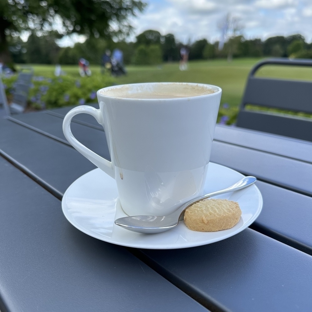 A cup of coffee with people golfing in the background.