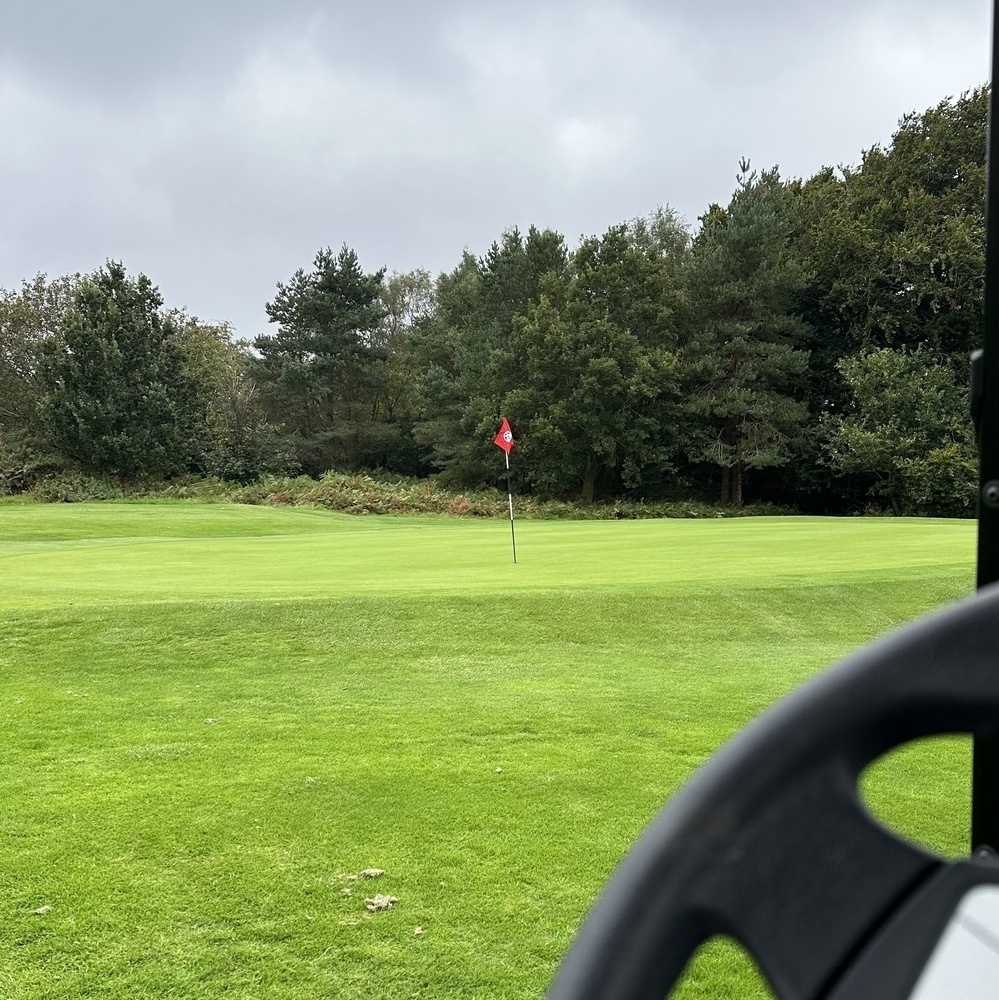 A golf course with a flag on the green is partially visible from inside a vehicle.