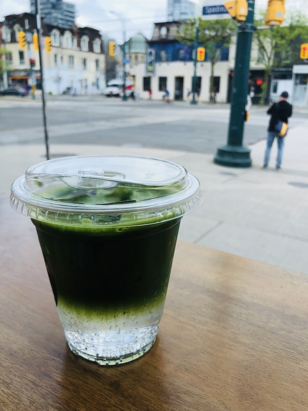 Matcha with tonic water in a transparent cup on a table looking at the corner of Nassau and Spadina in Toronto.