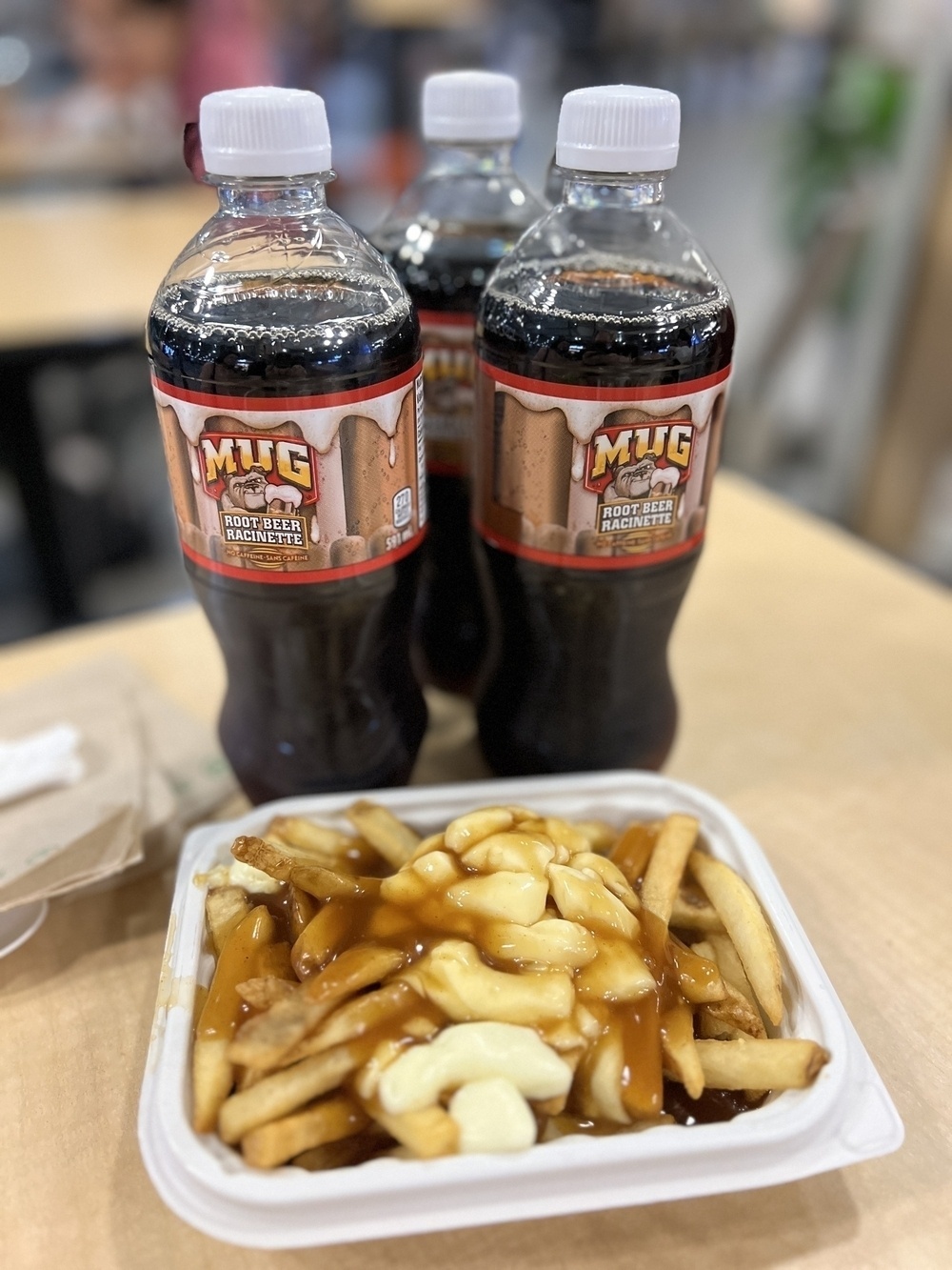 A bowl of fresh poutine and 3 bottles of Mug Root Beer