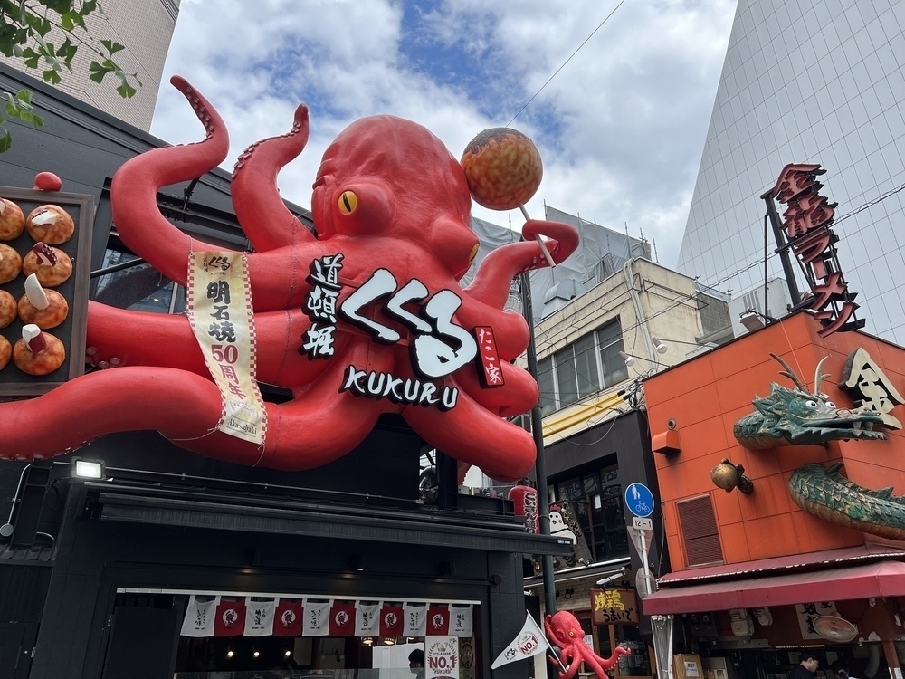 Giant 3D octopus on the side of a takoyaki shop. In the background is another sign with a dragon looking like it is wending its way in and out of a ramen shop