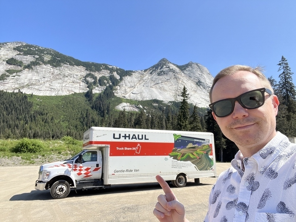 Chad selfie in front of a 26 foot U-Haul truck. In the background are some stark looking mountain tops