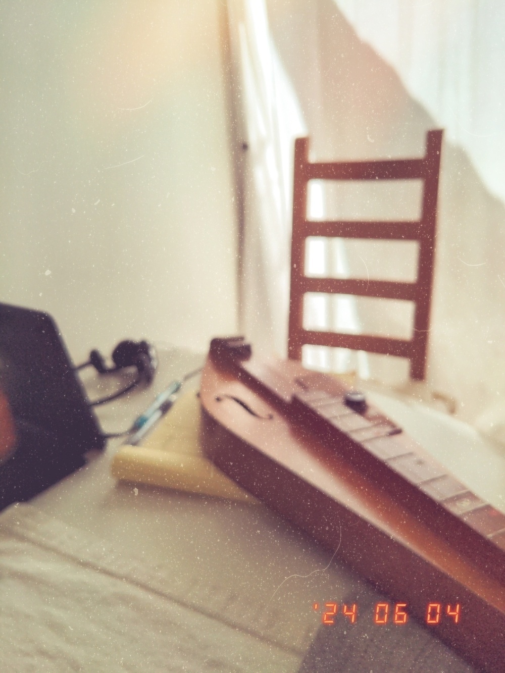 A dulcimer, a notebook, and a tablet on a table next to a wooden chair with sunlight streaming through a curtained window. The date "24 06 04" is visible in the corner.