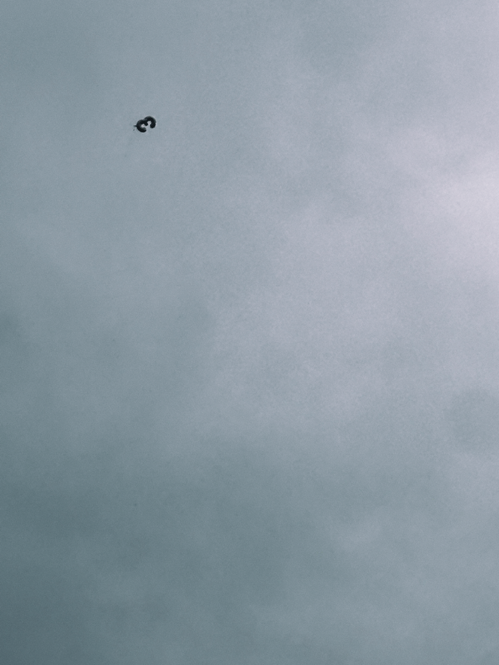 A small balloon in the shape of an inverted number three, against the expanse of the grey, cloudy sky.