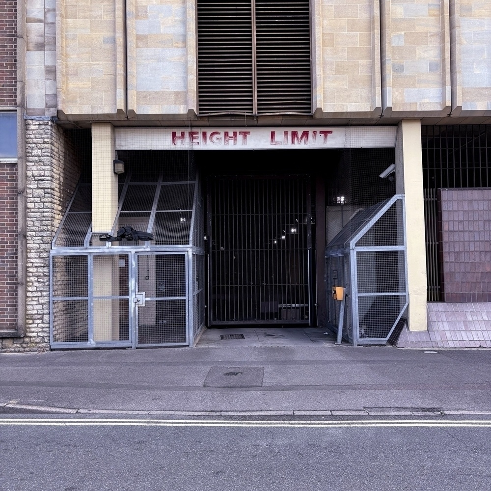 Auto-generated description: A barred entrance with mesh-enclosed sides and a HEIGHT LIMIT sign above it is seen from a street.