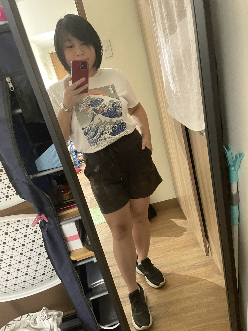 Chi showing her outfit for the day, which is a white shirt top with a print of the Kanagawa Waves, black shorts, and black rubber shoes.