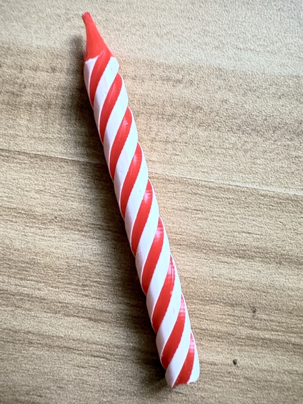 A red and white-striped birthday candle on a wooden surface.