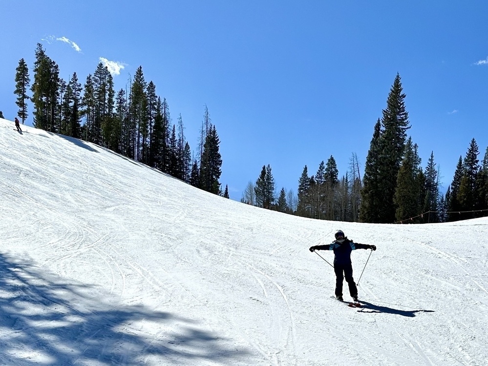 Meera celebrating on skis in front of clear blue skies.