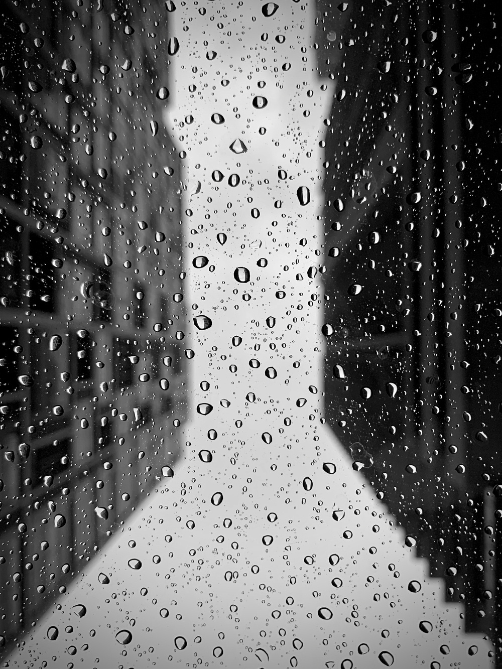 A view looking up from inside the car through the sunroof on a rainy evening. The glass roof has rain droplets and the buildings above are blurred.