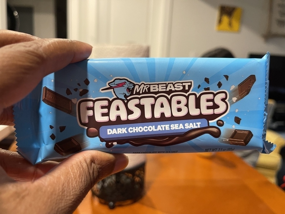 A hand is holding a bar of MrBeast Feastables dark chocolate sea salt flavor. 