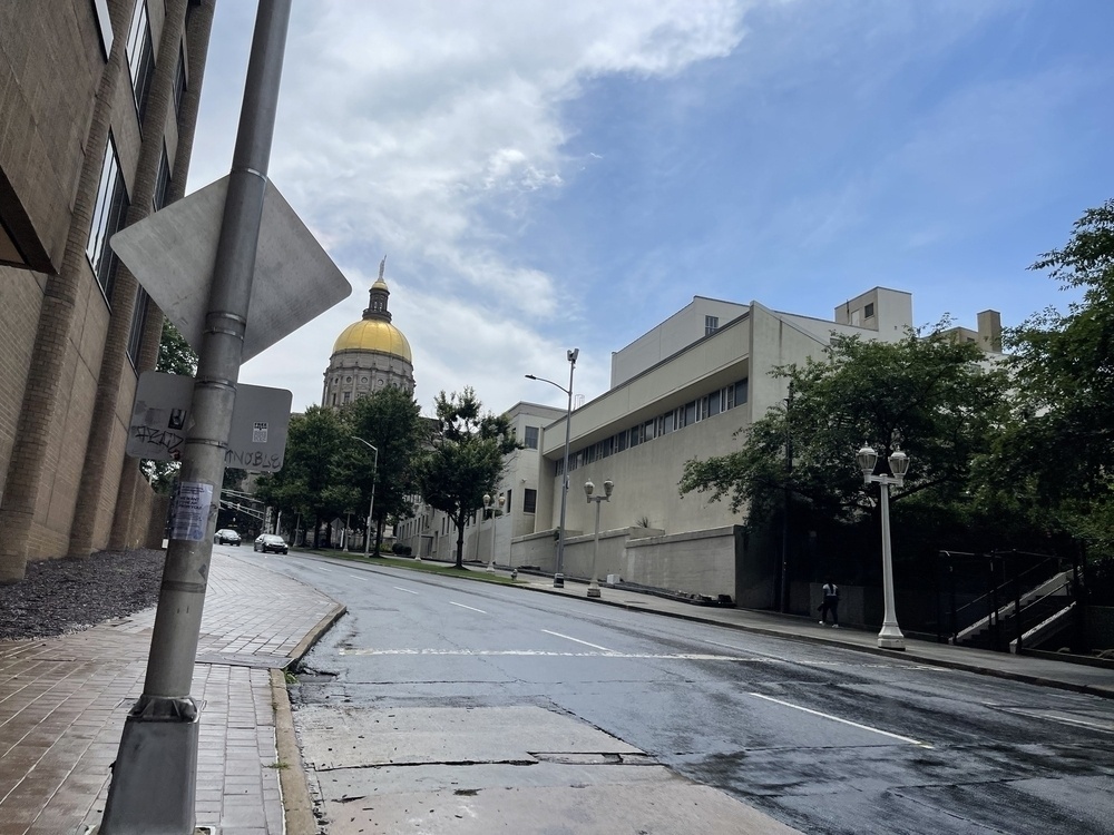 A street view shows a wet road with a building featuring a golden dome in the background under a partly cloudy sky.