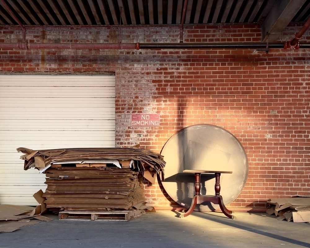 Parts of a table and cardboard stacked on a pallet placed on a loading dock. A “no smoking” sign is on the wall