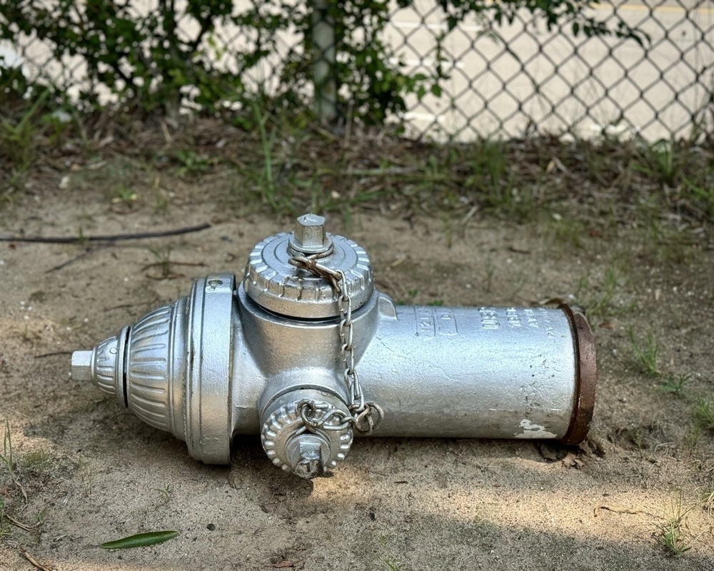 Silver fire hydrant, disconnected and on its side on the ground 