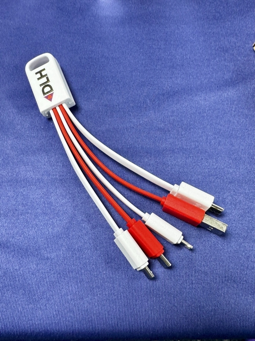 A multi-connector cable with red and white ends is laying on a blue fabric surface.