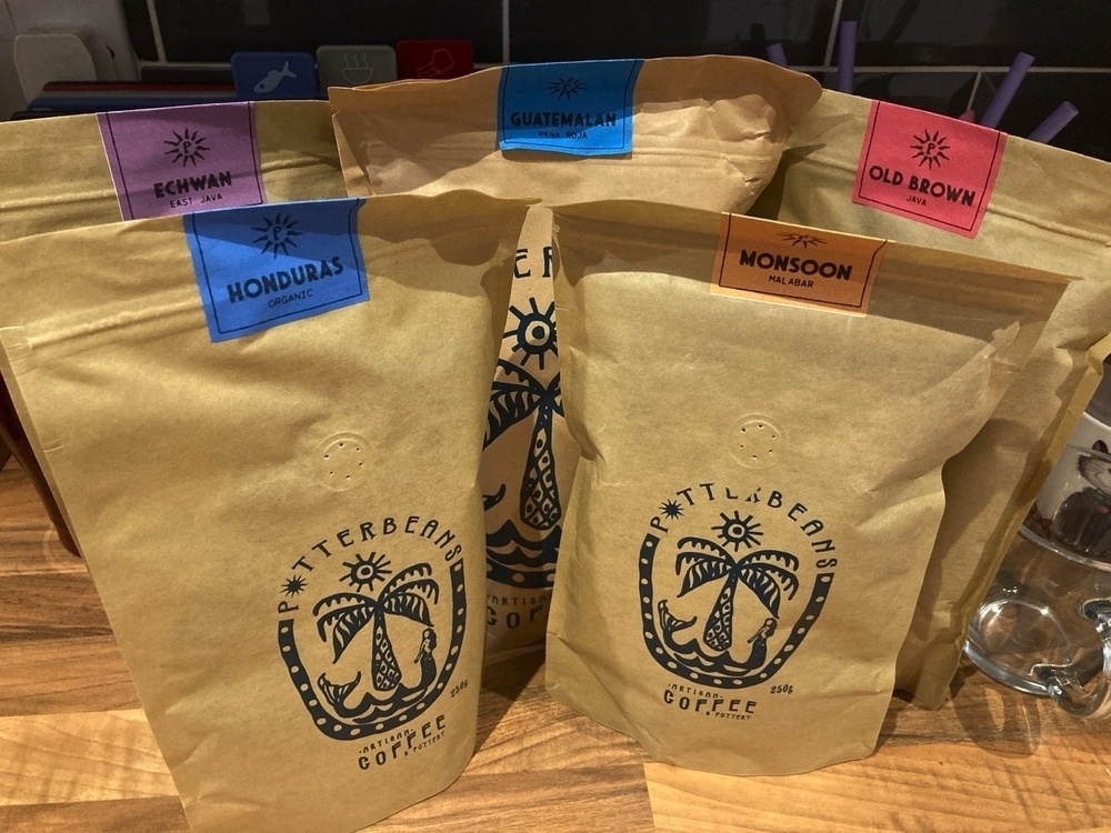 Five bags of coffee, on a kitchen counter-top. They are; Echwan (East Java), Honduras organic, Monsoon Malabar (Southern India), Old Brown (Java), and Guatemalan (Peña Roja).