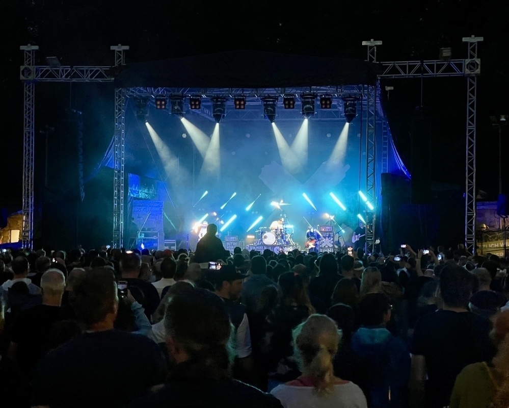 A crowd is gathered in front of an illuminated stage at night, watching a live music performance by Sportfreunde Stiller.